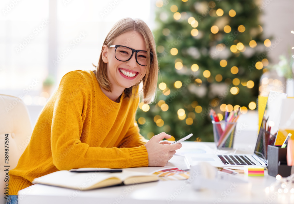 Happy  young woman freelancer laughs while sitting at a workplace with a phone in her hands in a hom