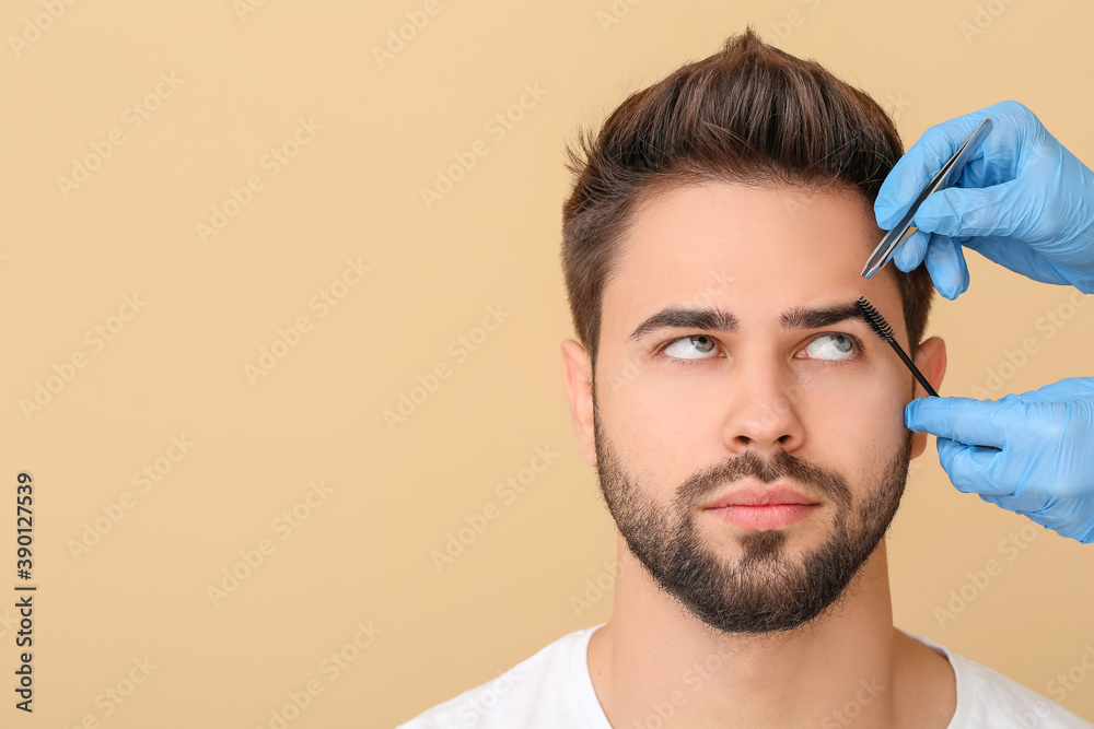 Young man undergoing eyebrow correction procedure on color background