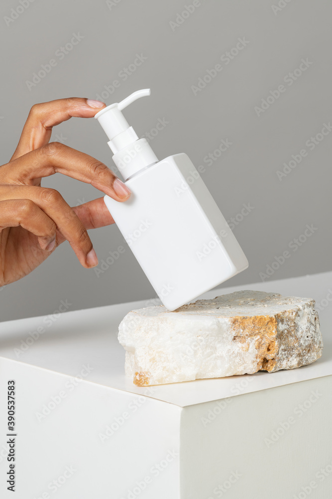 Hand arranging a blank white pump bottle on a stone