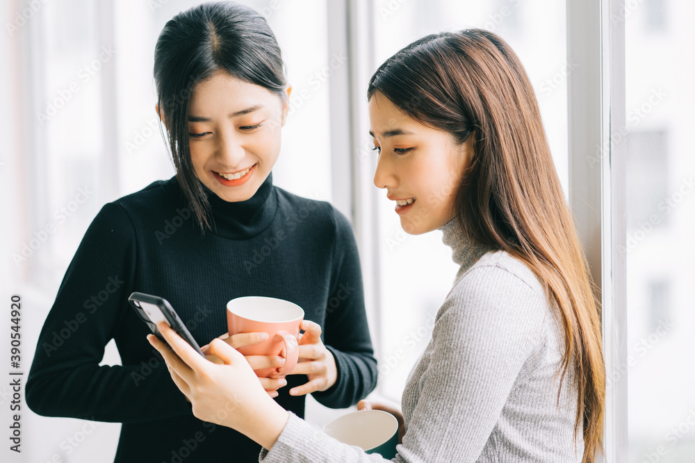 两名亚洲商界女性在课间休息时在窗户边聊天