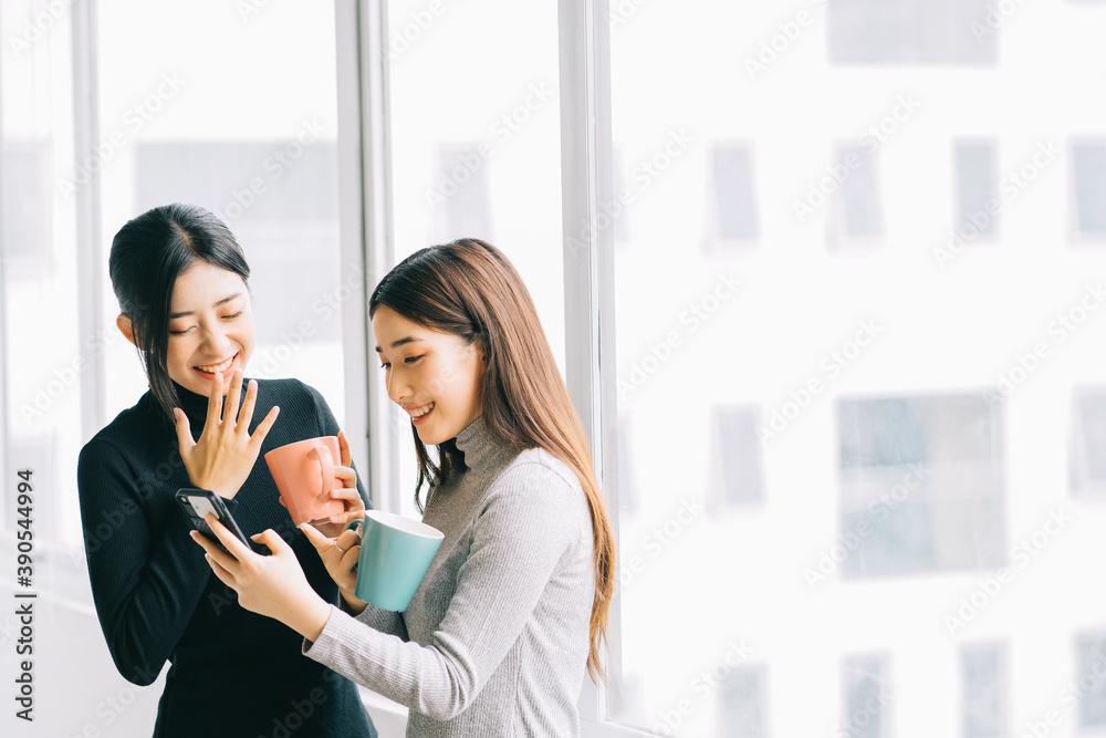 两名亚洲商界女性在课间休息时在窗户边聊天