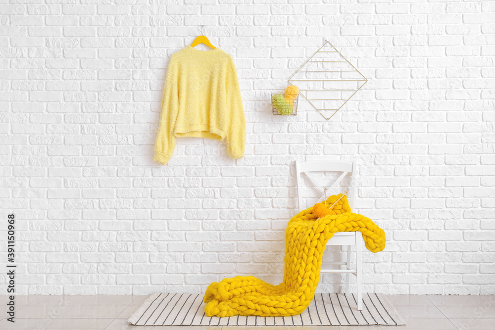 Chair with yellow plaid and knitting yarn near white brick wall