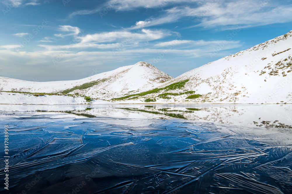 结冰的山湖，湖面有蓝色的冰和裂缝。冬季雪景如画