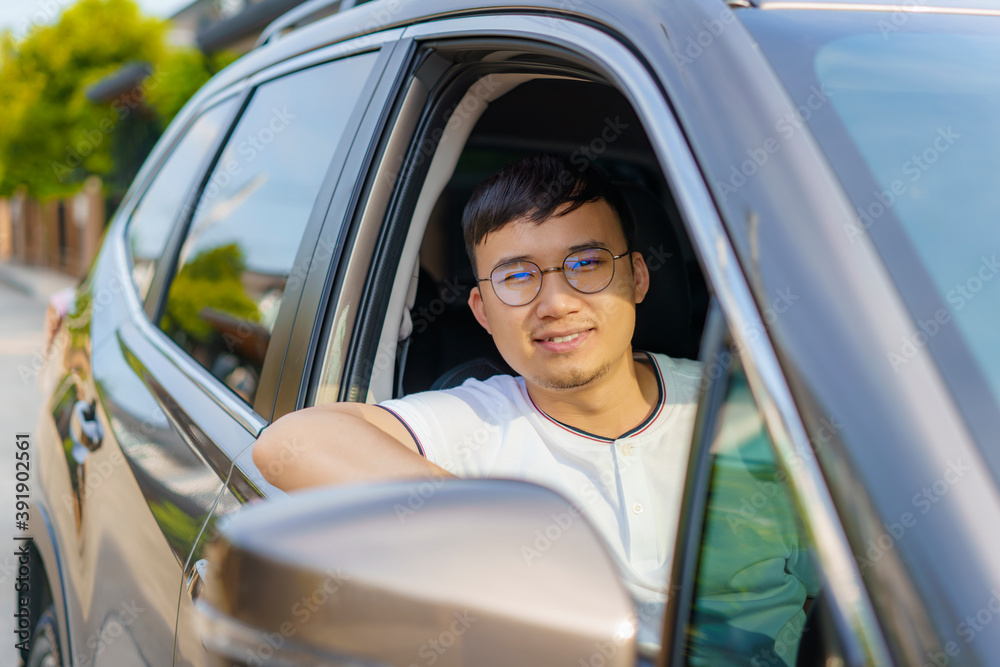 亚洲快乐的年轻英俊男子微笑着驾驶汽车，带着他的ca准备旅行