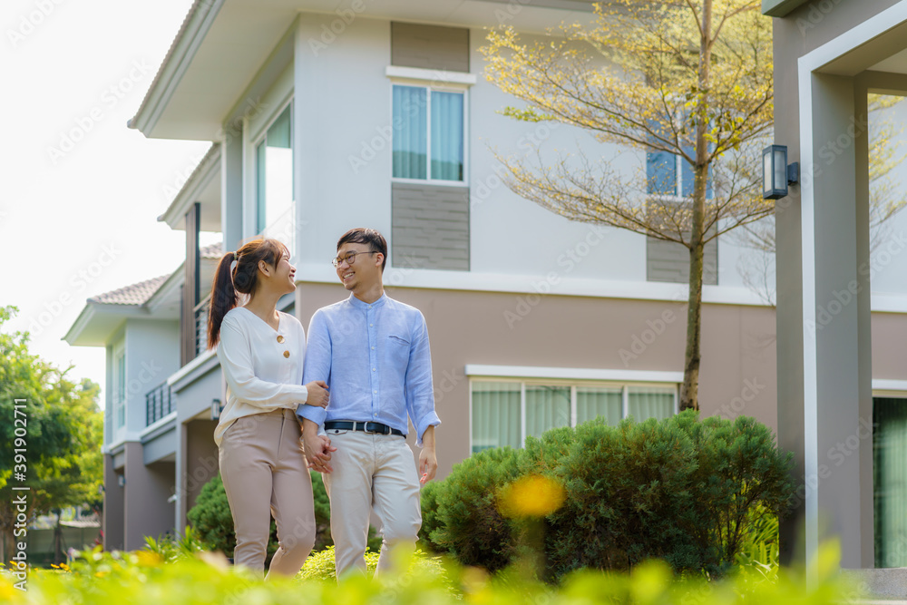 Portrait of Asian couple walking and hugging together looking happy in front of their new house to s