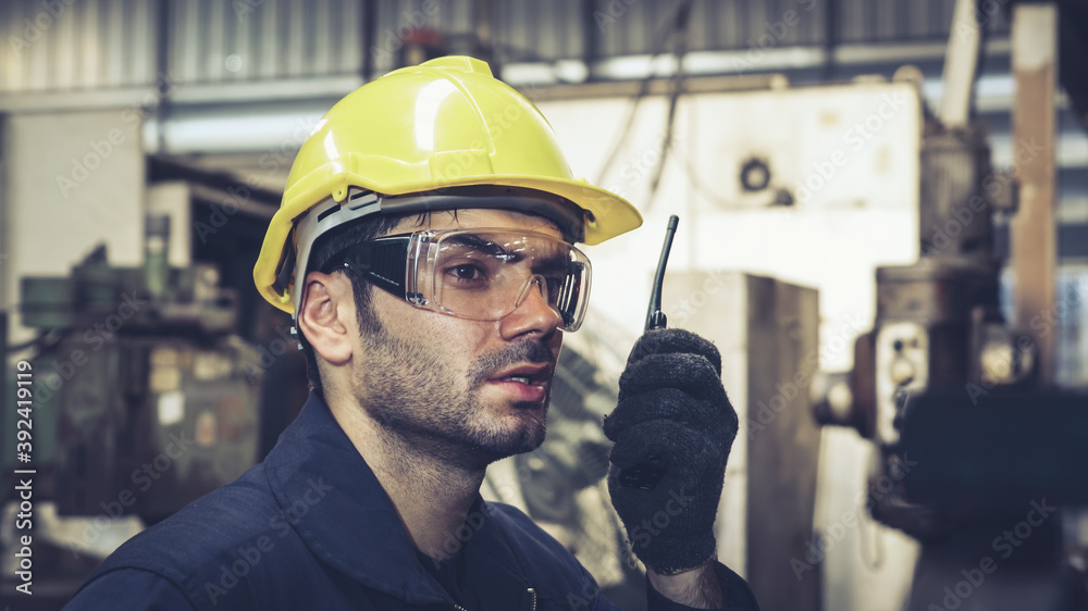 Factory worker talking on portable radio while inspecting machinery parts . Industrial and engineeri