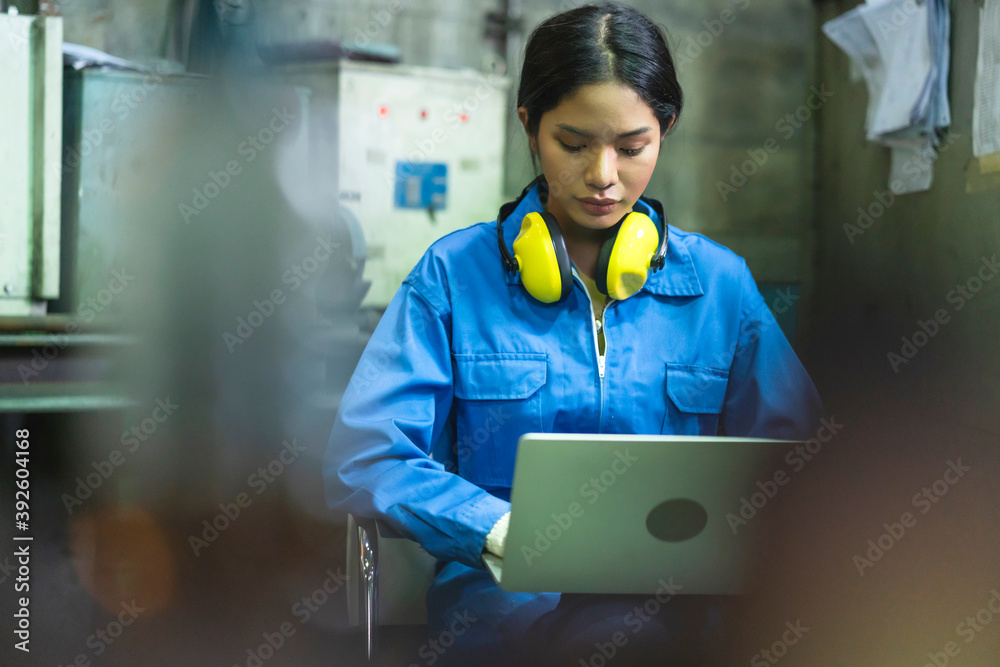 asian female engineer in safty uniform hand use latop checking operation process in factory workshop