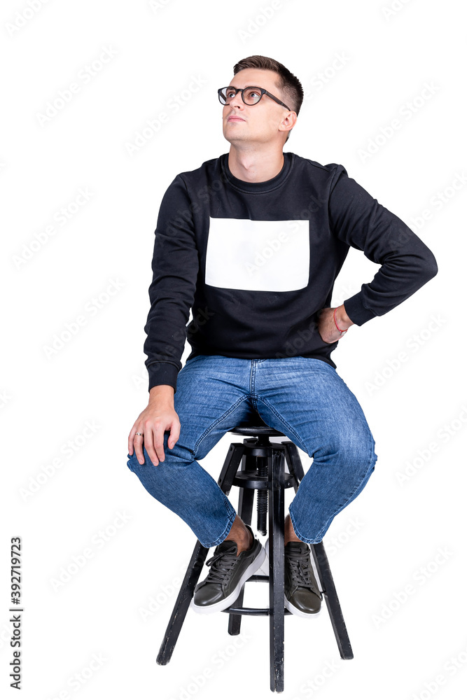 Model man presents modern glasses. Male sits on high bar chair in casual sweater and blue jeans.