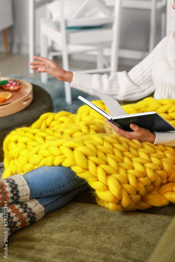 Beautiful young woman with warm plaid reading book at home