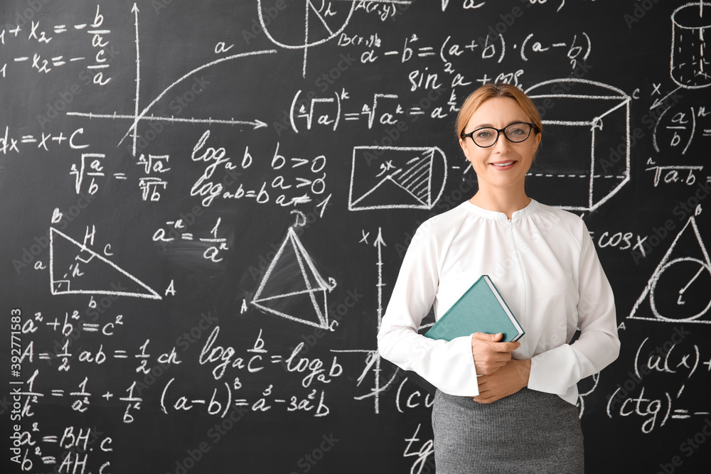 Mature maths teacher near blackboard in classroom