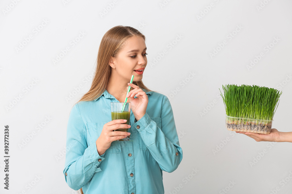 Young woman with wheatgrass juice on light background