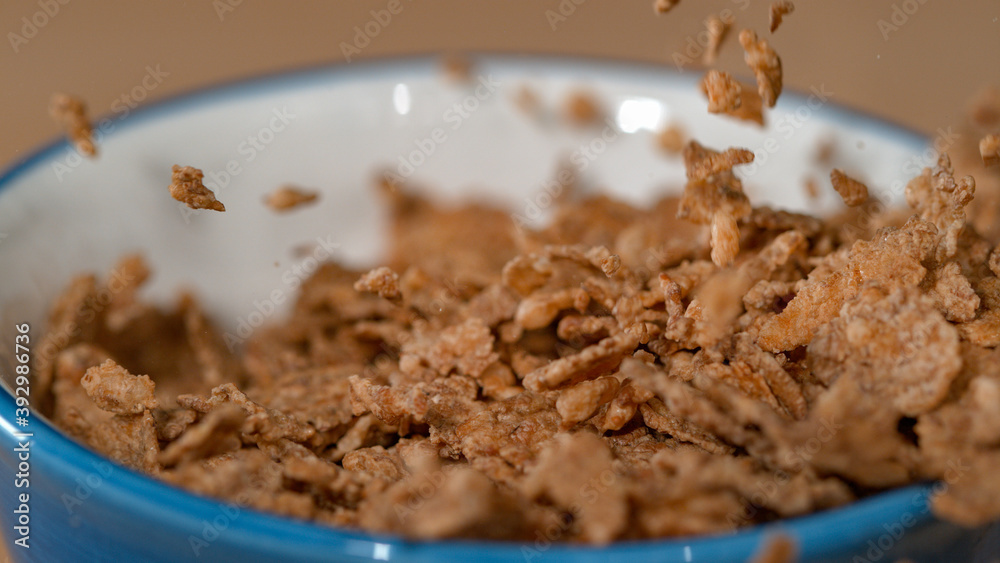 MACRO: Healthy whole grain breakfast cereal flakes fall into an empty bowl.