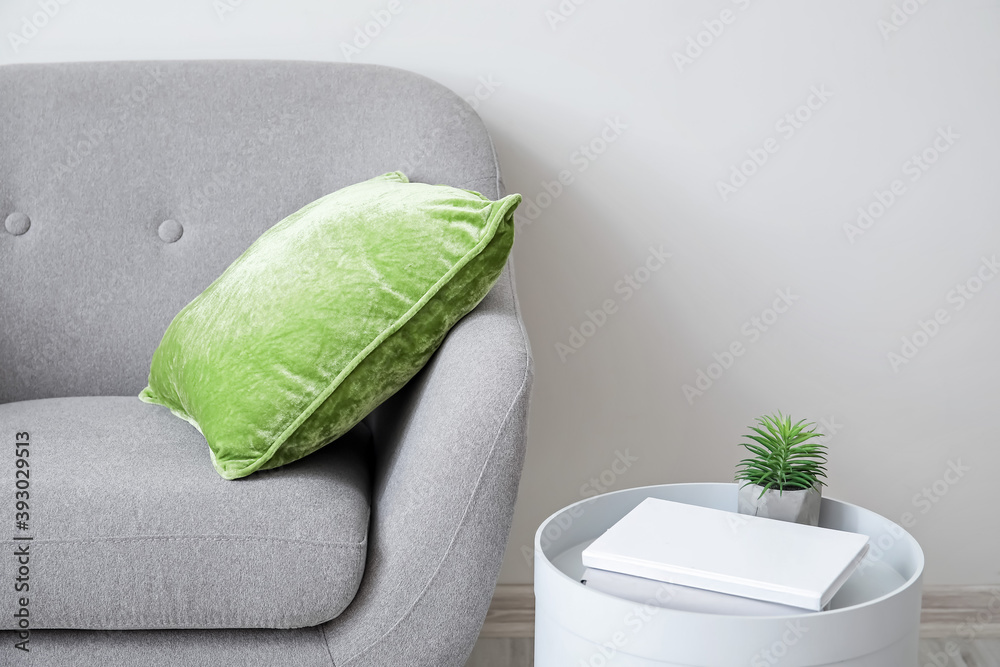 Stylish armchair with pillow and table with book near light wall in room