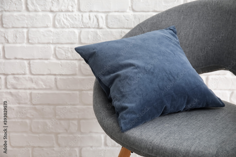 Stylish armchair with pillow near brick wall in room