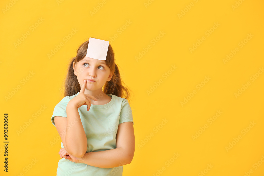 Thoughtful little girl with blank note paper on her forehead against color background