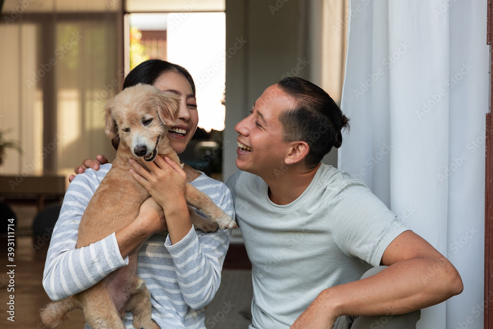 多元化年轻夫妇在家里和他的狗玩耍。他们拥抱着他们的小狗