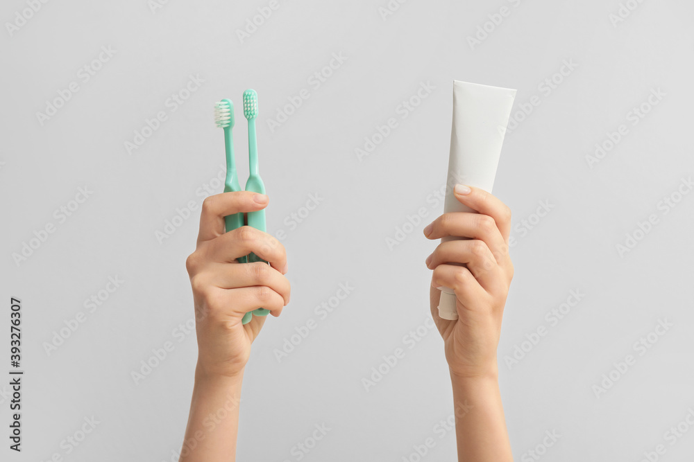 Female hands with toothbrushes and paste on light  background