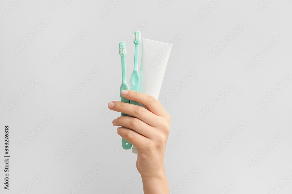 Female hand with toothbrushes and paste on light  background