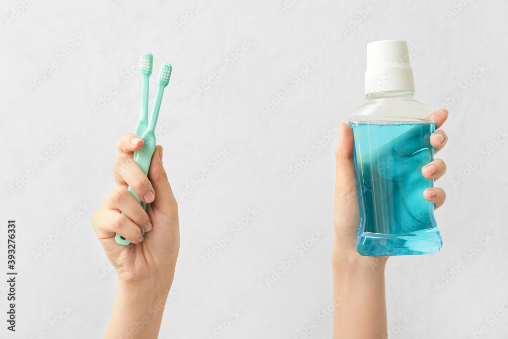 Female hands with toothbrushes and mouth rinse on light background