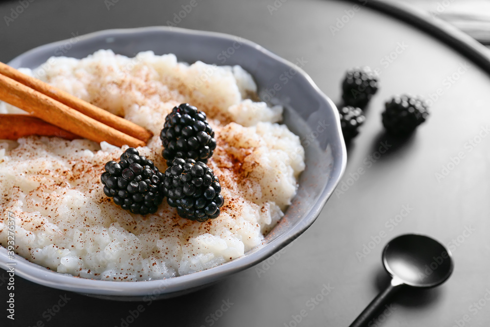 Plate of tasty rice pudding with blackberry and cinnamon on black tray