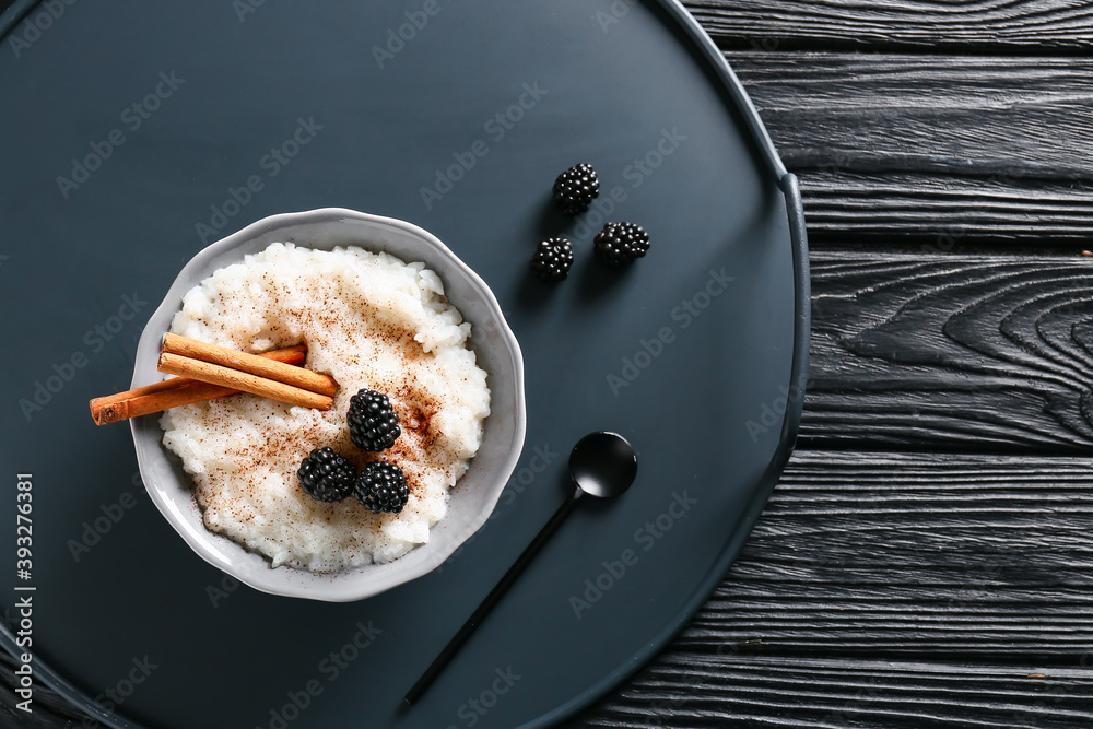 Plate of tasty rice pudding with blackberry and cinnamon on black tray