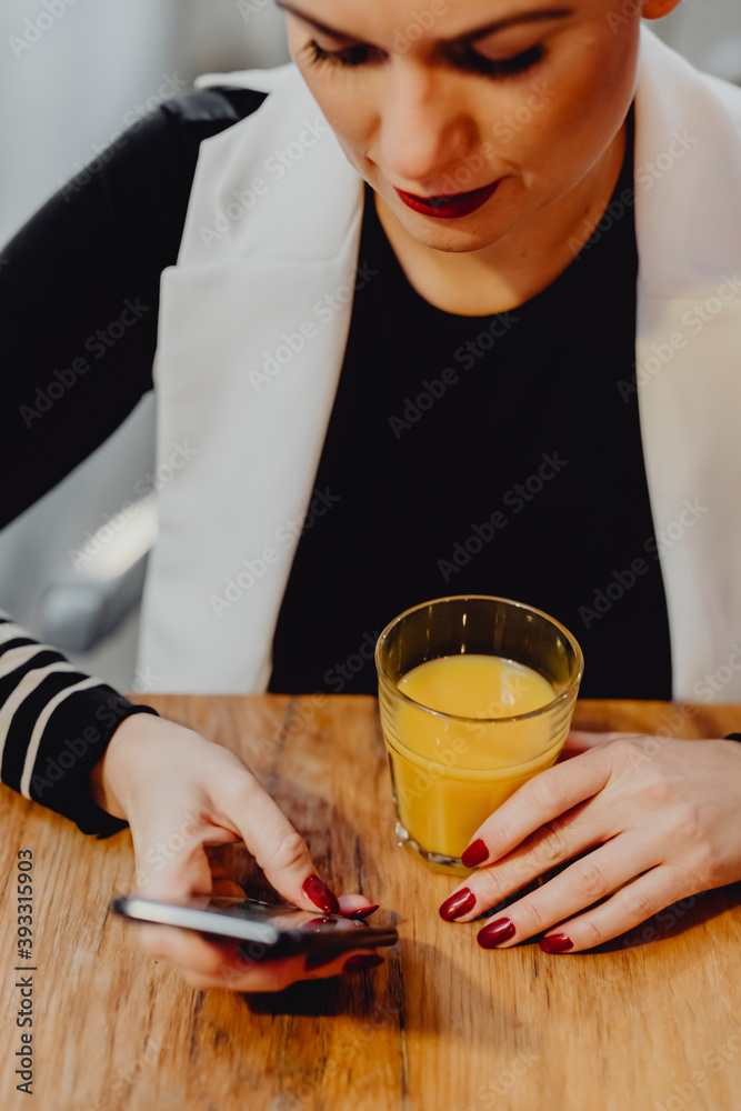 一个女人正在喝一杯果汁并检查她的手机