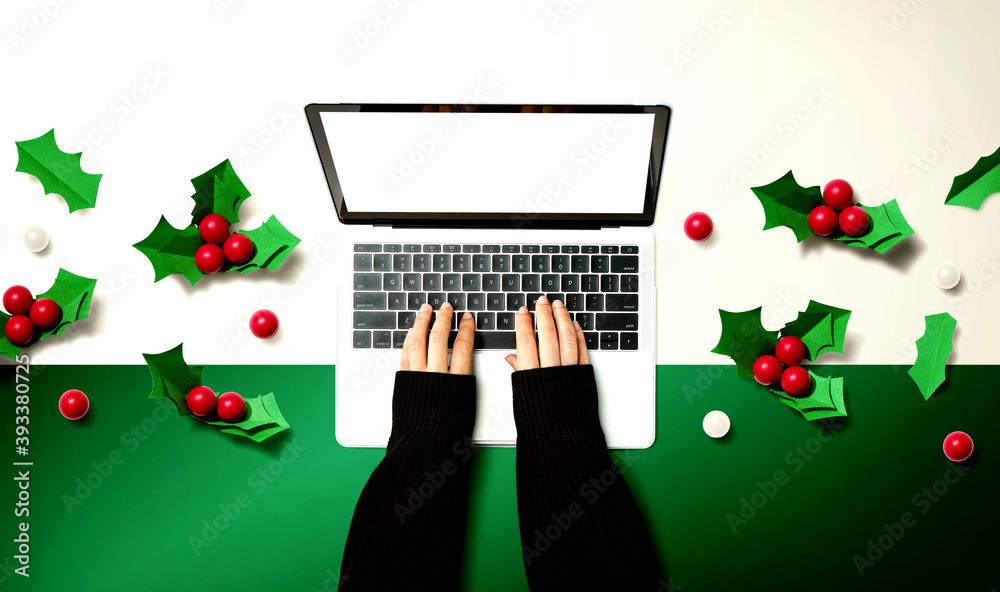 Person using a laptop computer with Christmas holly berries from above