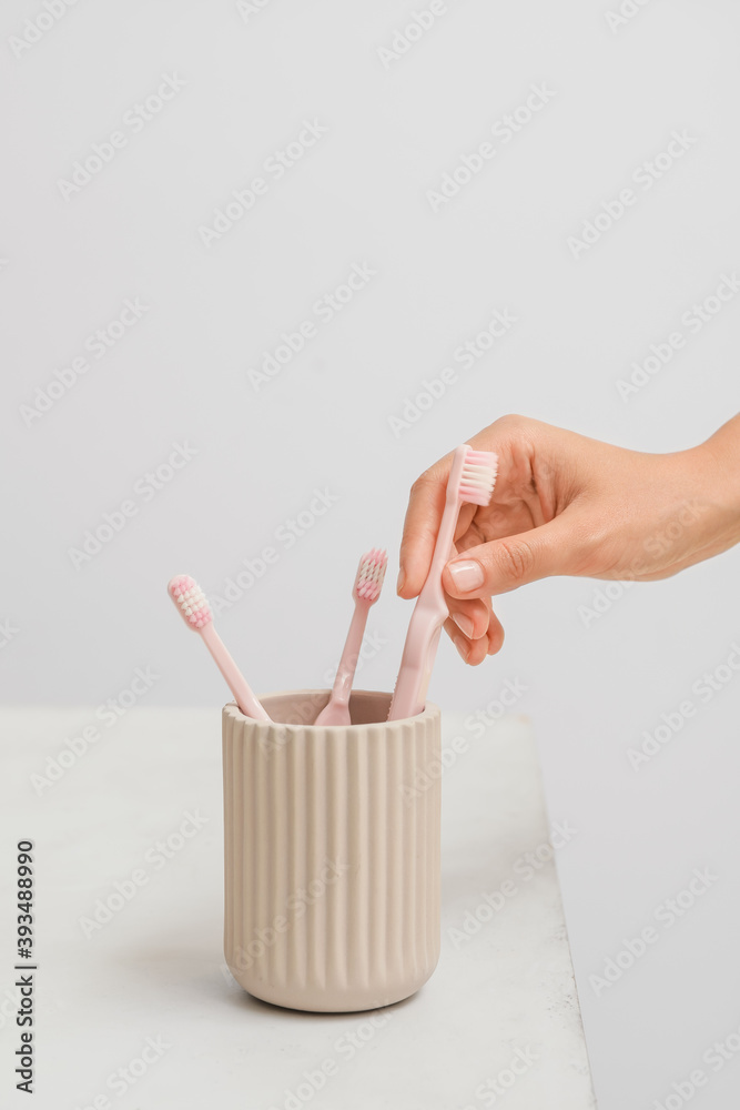 Woman taking pink toothbrush from holder in bathroom