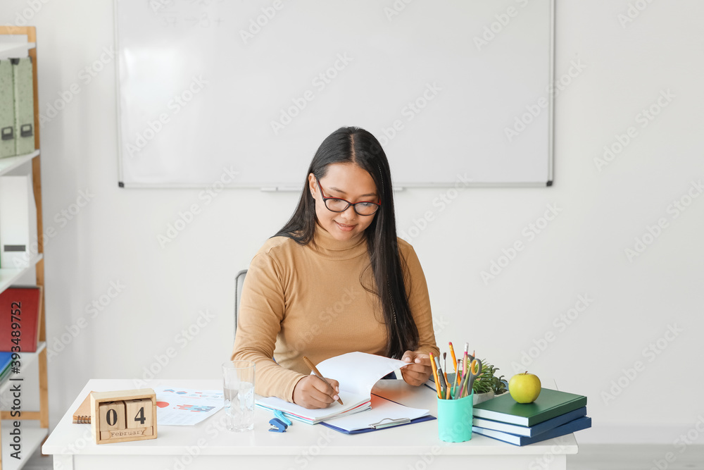 亚洲女教师坐在教室的桌子旁