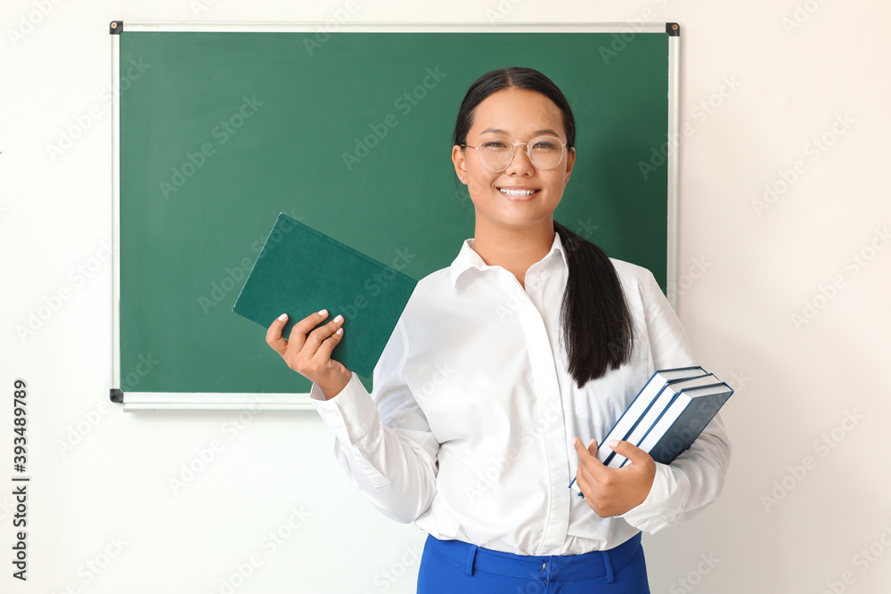 Asian female teacher near blackboard in classroom