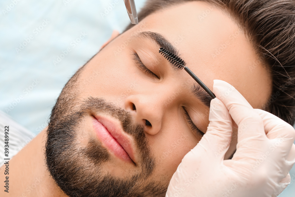 Young man undergoing eyebrow correction procedure in beauty salon