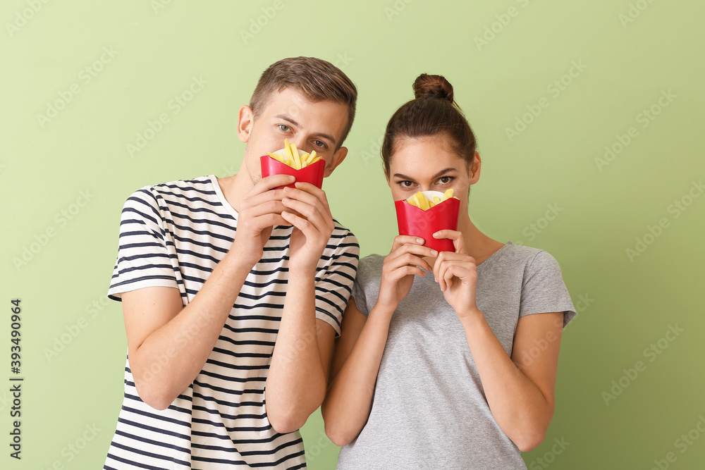 Young couple with french fries on color background