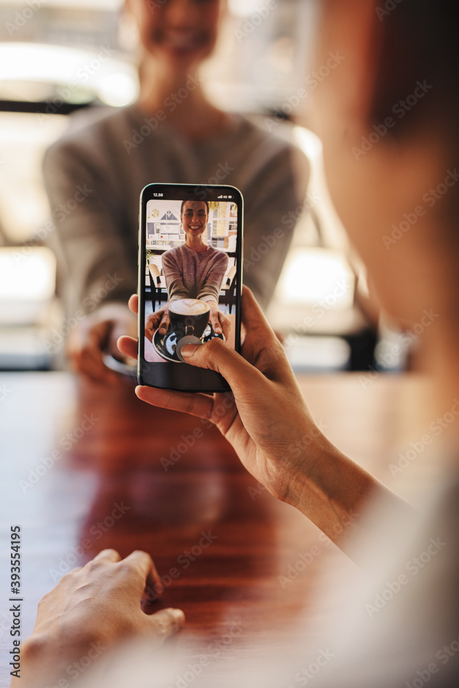 Woman photographing her friend in coffee shop