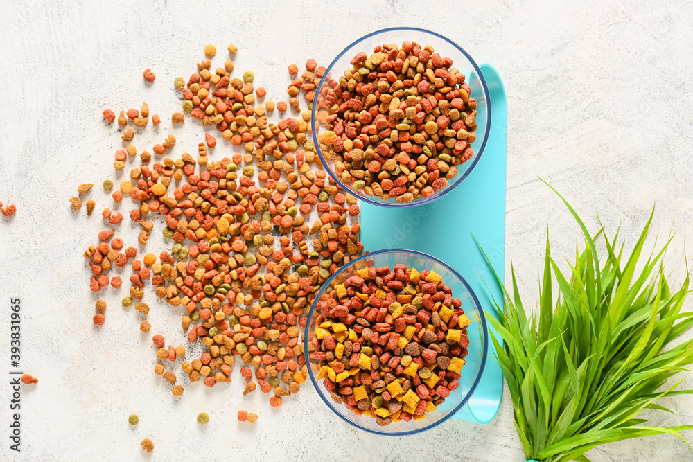 Bowls with dry pet food and grass on light background