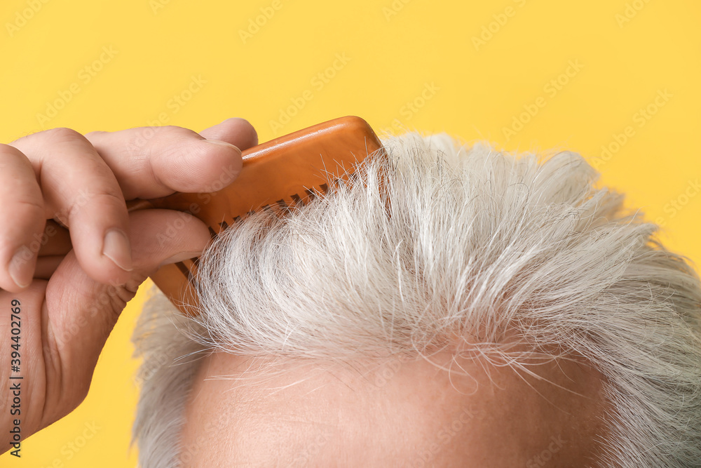 Senior man combing his hair on color background, closeup