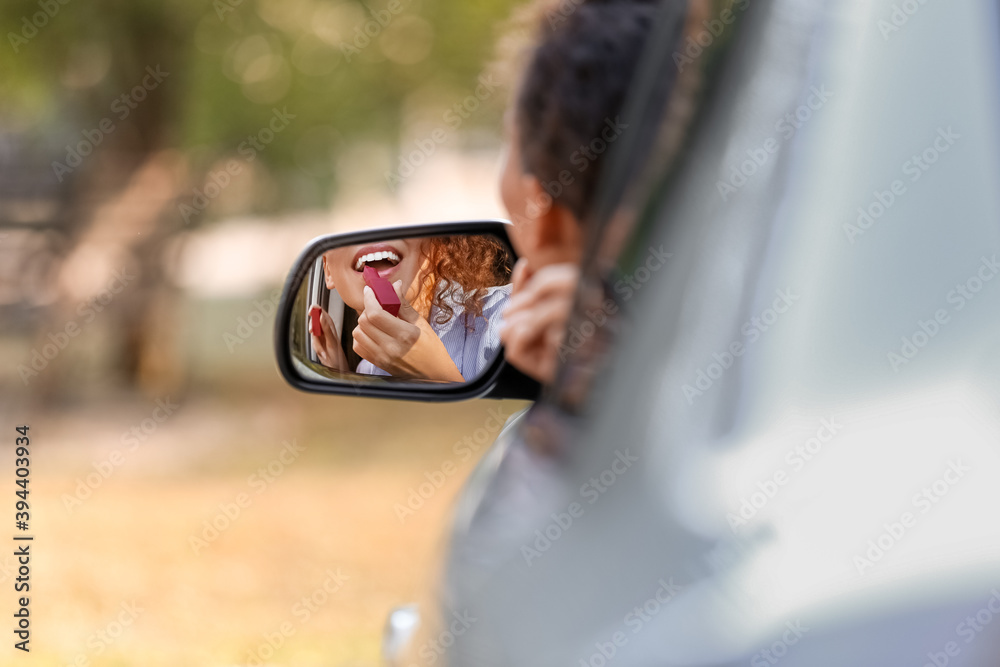 Beautiful African-American woman applying lipstick while sitting in car