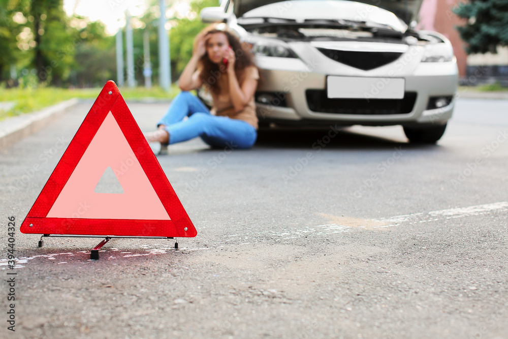 Emergency stop sign and stressed African-American woman near broken car outdoors