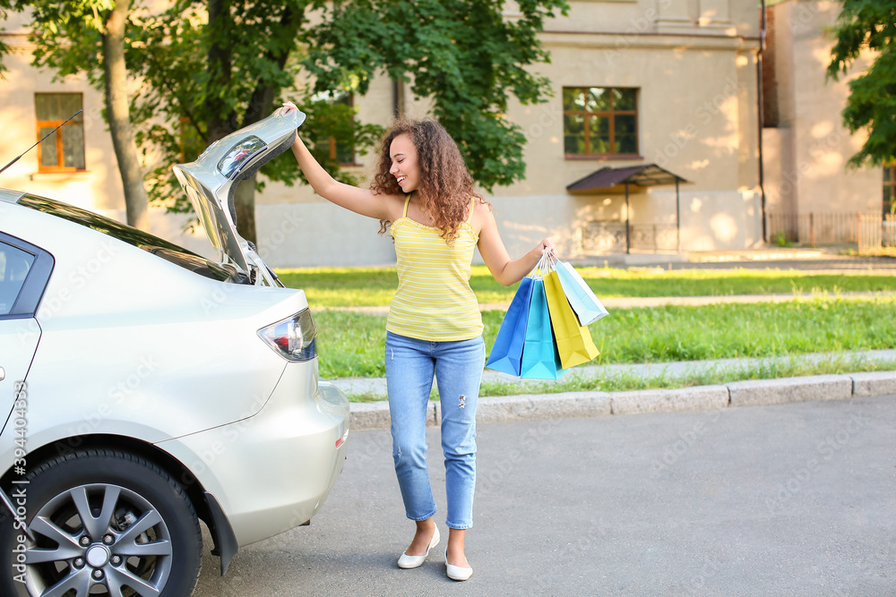 African-American woman with shopping bags near car outdoors