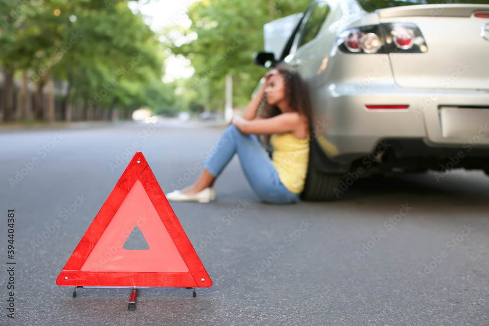 Emergency stop sign and stressed African-American woman near broken car outdoors