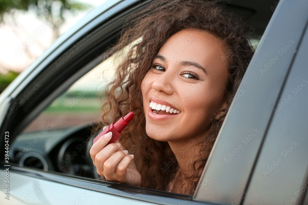 Beautiful African-American woman applying lipstick while sitting in car