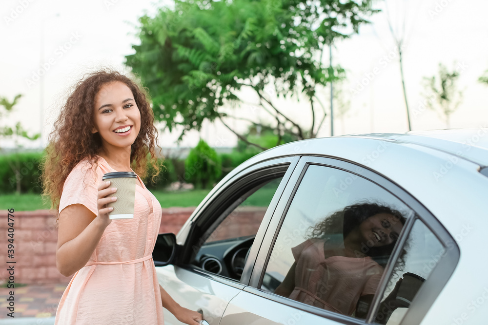 Young African-American woman with coffee near car