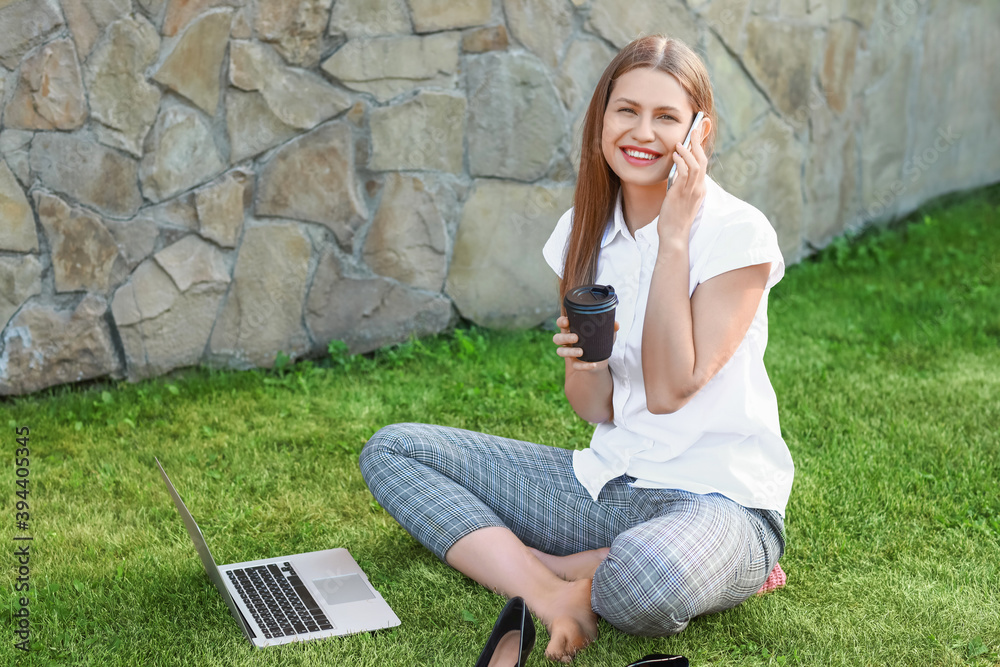 Beautiful young businesswoman with laptop talking by phone in park