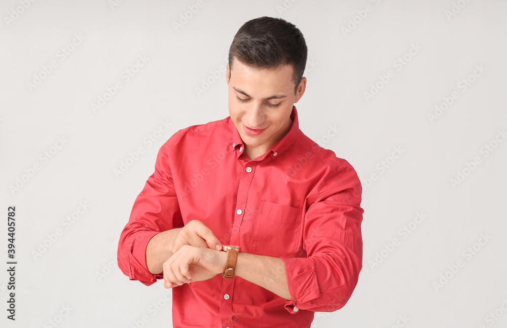 Young man with wristwatch on light background