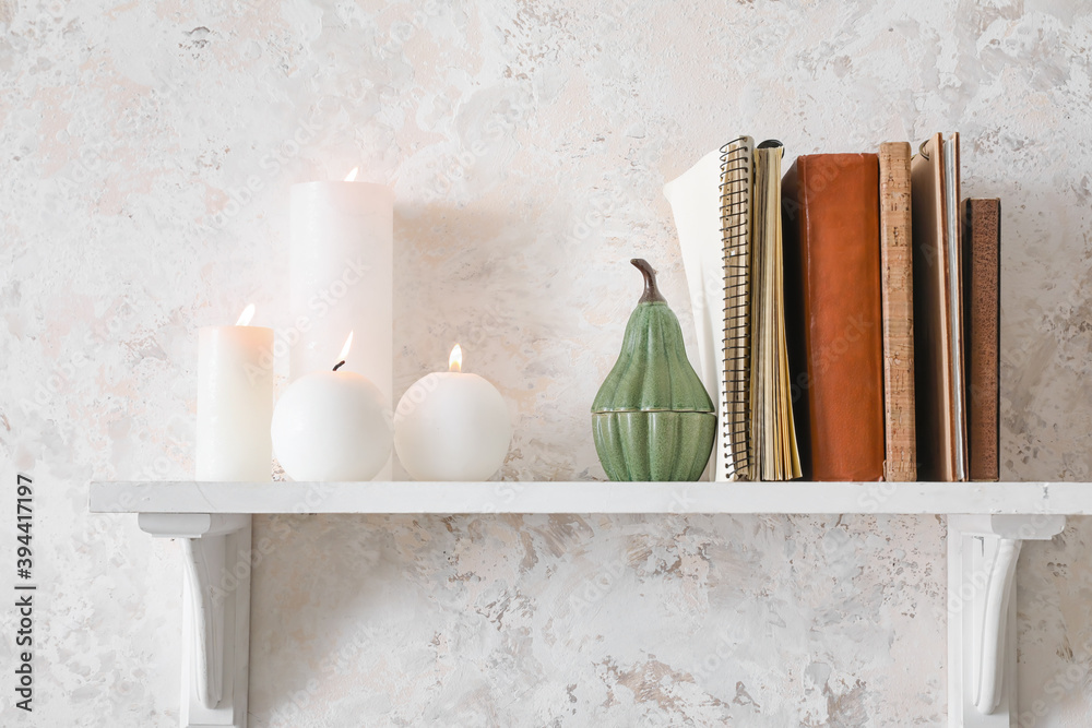 Shelf with burning candles on wall in room