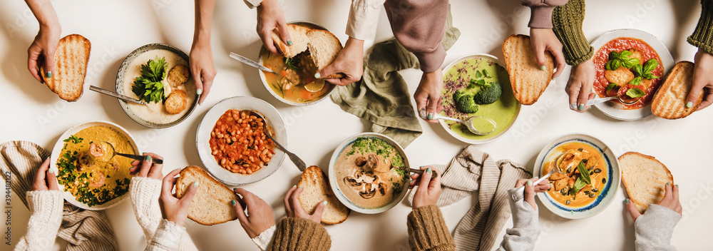 人们在吃秋冬季奶油素食汤。人们的手、汤盘和面包都是平放的