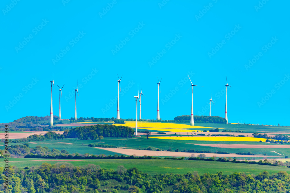 Group of white wind power turbine generators rotate in an agricultural field in Germany, Europe