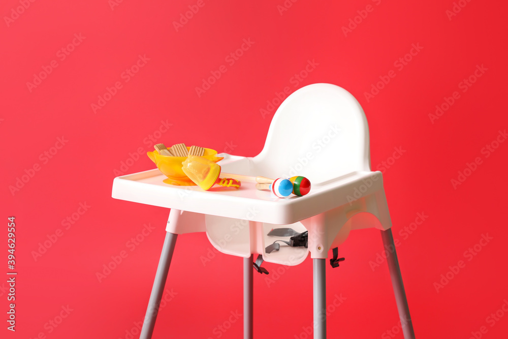 Baby highchair with food and toy on color background