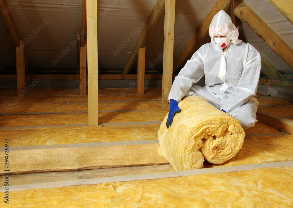 Worker thermally insulating house attic with glass wool