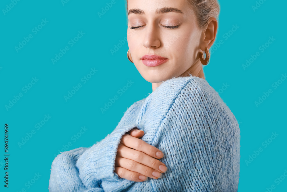 Beautiful young woman in warm sweater on color background