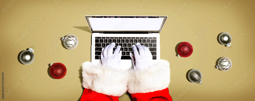 Santa Claus using a laptop computer with Christmas baubles from above